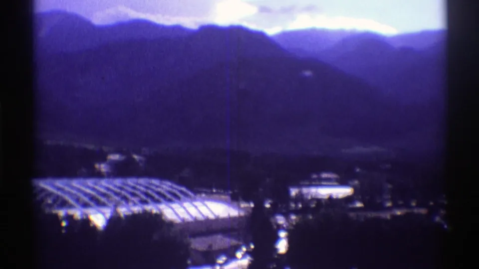 Colorado home-movie frame with a large curved roof, nearby lit structure, roads, and mountain slopes in blue-purple film color.