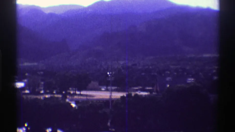 Colorado mountain ridge and small valley settlement in faded 8mm footage, with visible gate edge and soft archival focus.