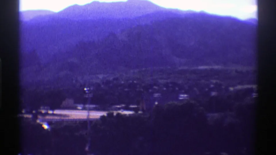 Faded 1969 Colorado home-movie frame with a forested mountain backdrop, valley buildings, and visible 8mm scan edges.