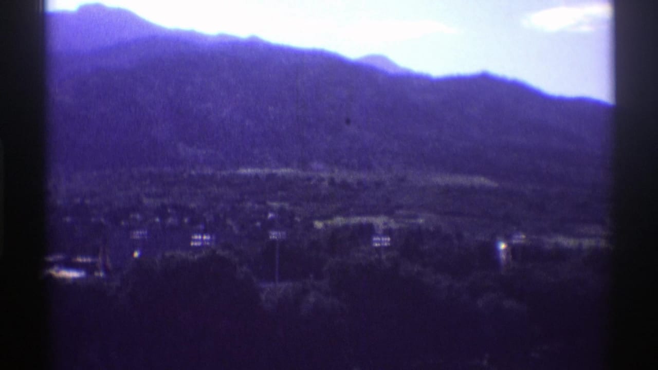 1969 Colorado 8mm frame showing a dark mountain silhouette, bright sky, trees, and distant lakeside structures.