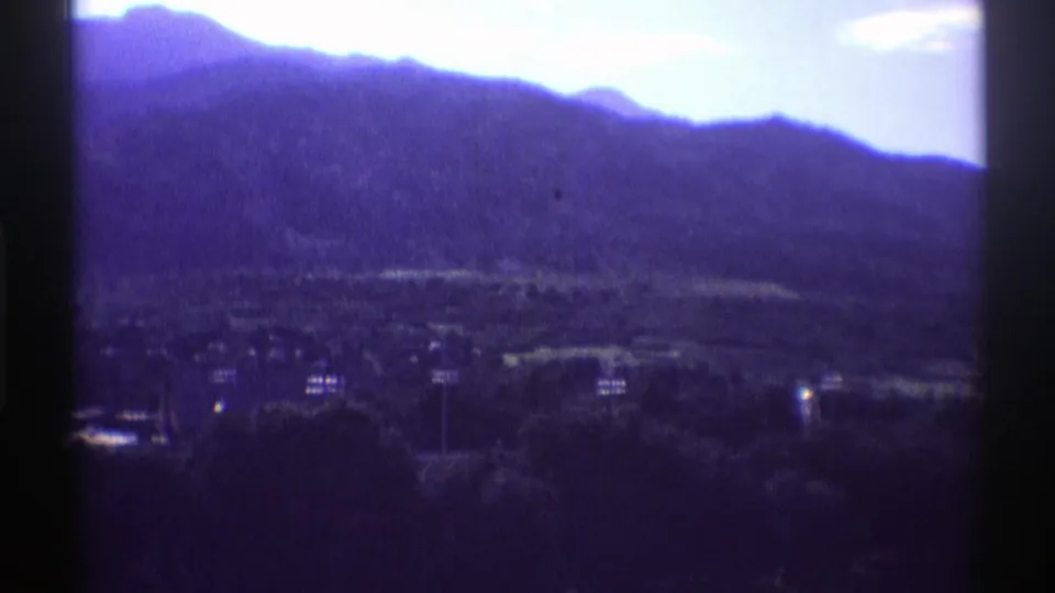 1969 Colorado 8mm frame showing a dark mountain silhouette, bright sky, trees, and distant lakeside structures.