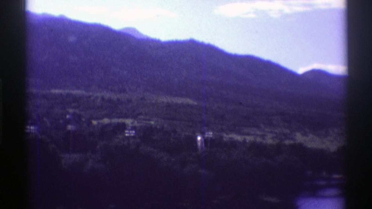 Mountain slope and wooded shoreline with small distant buildings under a bright sky.