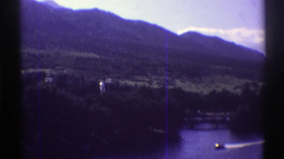 1969 Colorado 8mm frame showing lake water, a small speedboat wake, wooded shore, and mountain ridges.