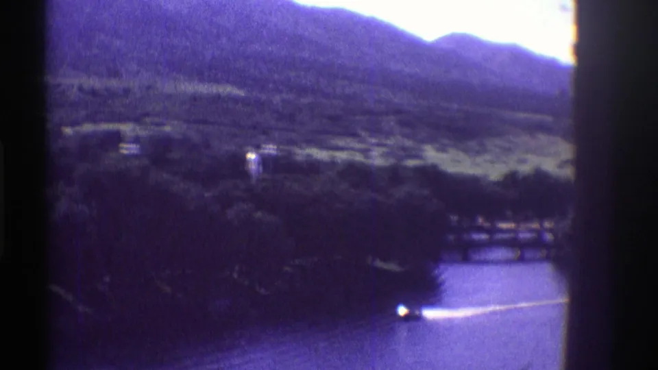 1969 Colorado home-movie frame with a speedboat moving across the lake, wooded shore, and mountains behind it.