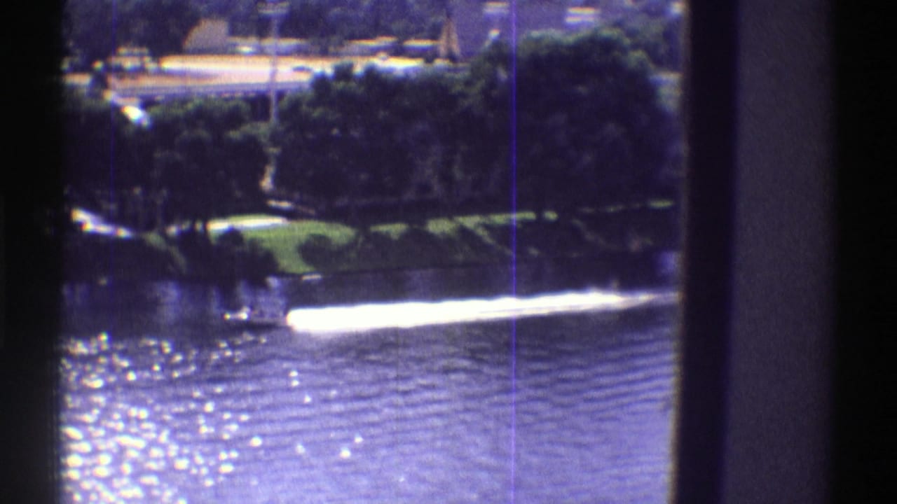 Motorboat wake crossing a sunlit lake behind dark window mullions.