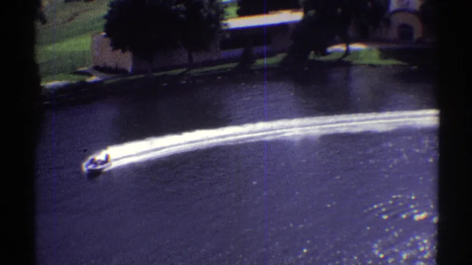 The boat turns across the Colorado lake, creating parallel white wake lines against dark water and a shaded shoreline.