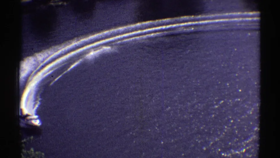 The speedboat moves partly out of frame as layered white wakes curve over the dark lake surface in this vintage Colorado home movie.
