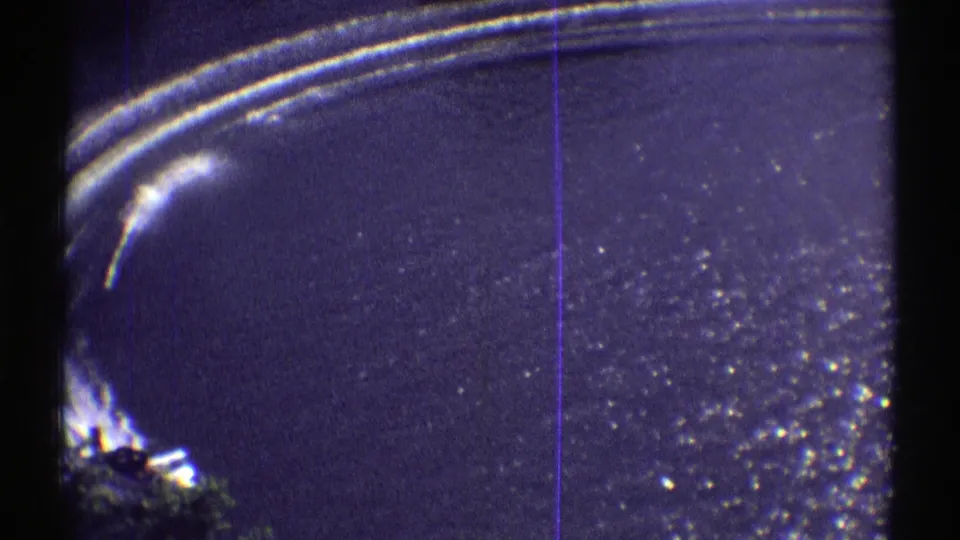 1969 Colorado 8mm frame showing a bright curved wake across a lake, with grain, fading, and dark frame edges visible.