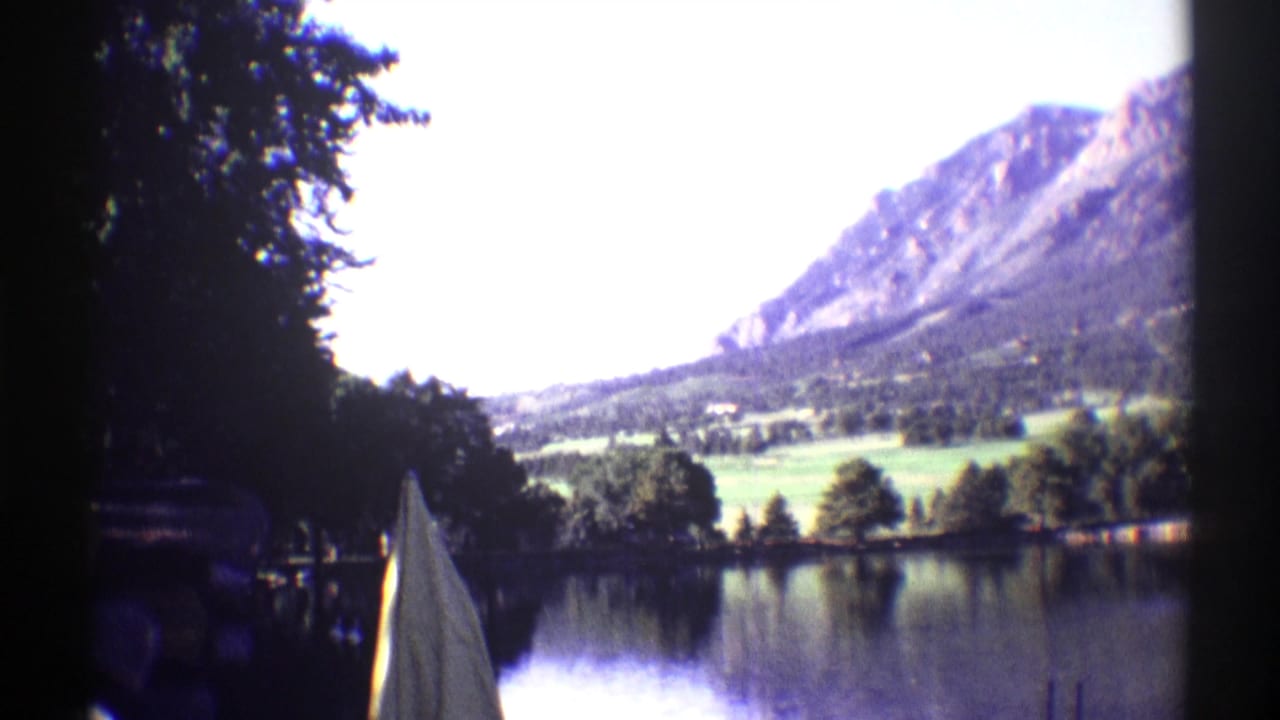 Mountain lake view with trees, shoreline, and a white shape near the water.