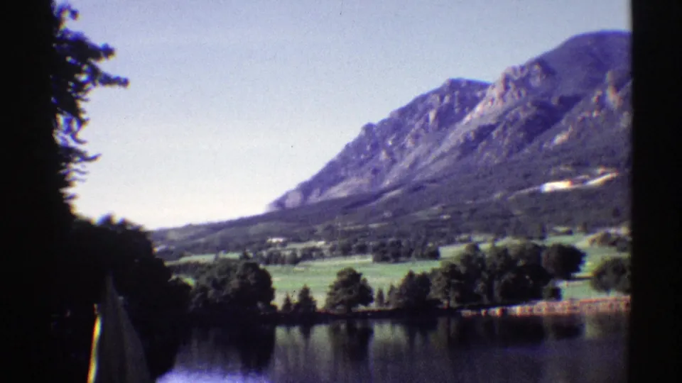1969 Colorado 8mm frame showing a broad brown mountain above green trees and a quiet lake shore.