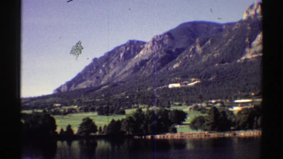 1969 Colorado 8mm frame of a mountain lake landscape with trees, open sky, and visible dust and vertical film marks.