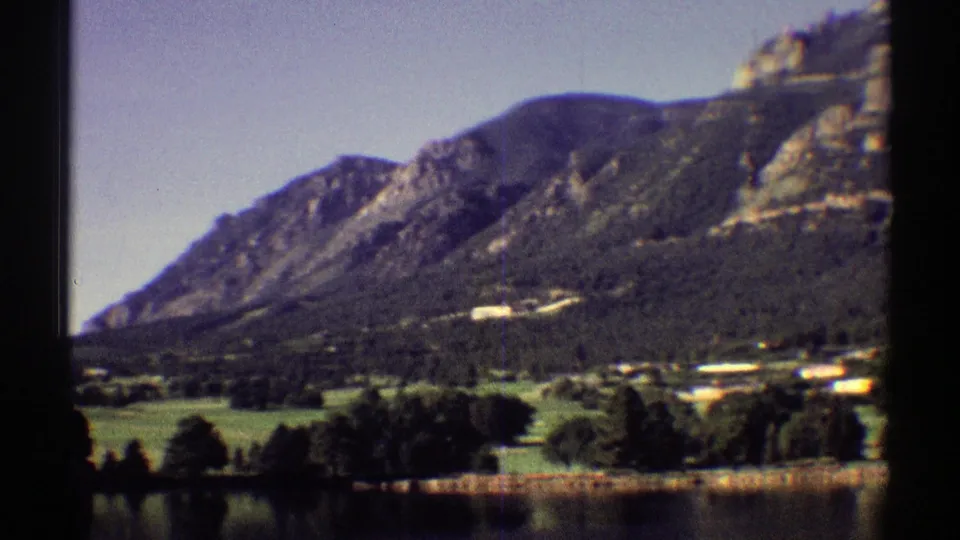 1969 Colorado 8mm frame showing a forested mountain slope, grassy valley, scattered lakeside houses, and still water.