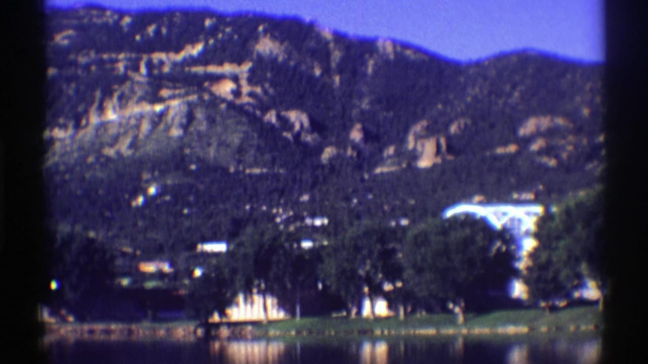 Mountain ridge above a lake shore with trees and small buildings.