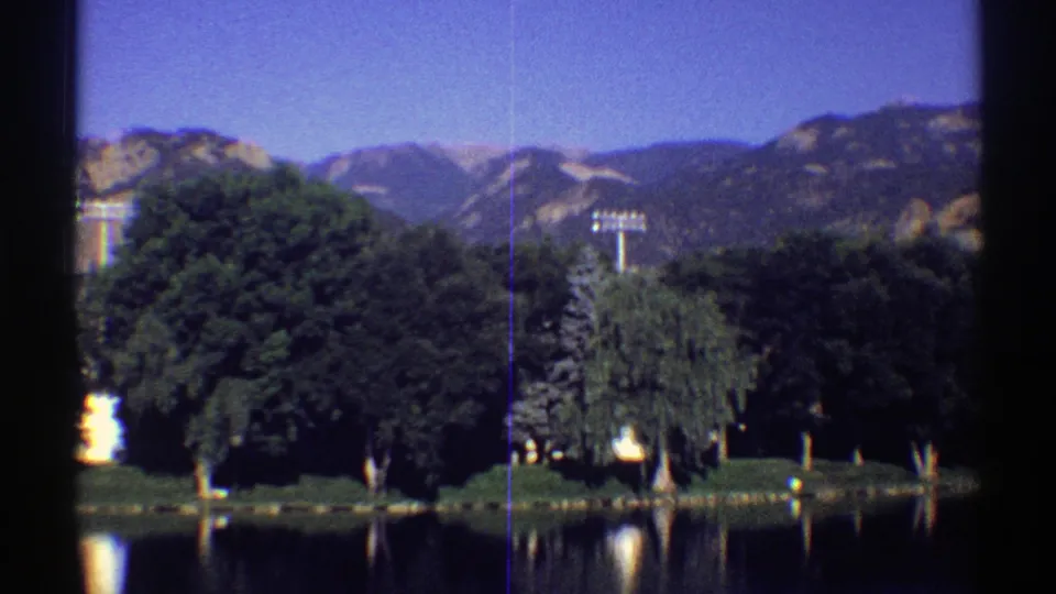 1969 Colorado 8mm frame showing a forested lake edge, distant mountains, and soft reflected light on the water.