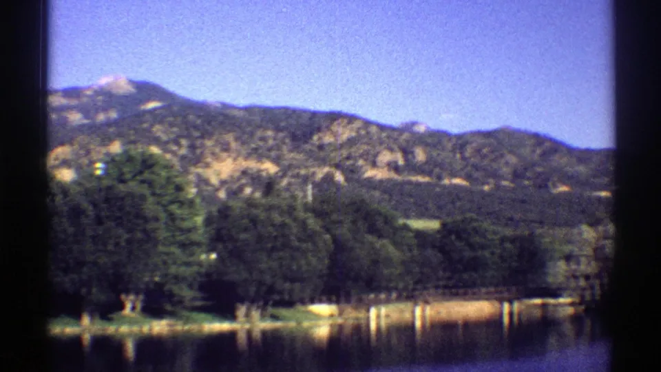 1969 Colorado 8mm frame with a wider view of lake water, shoreline trees, and sunlit mountain slopes.