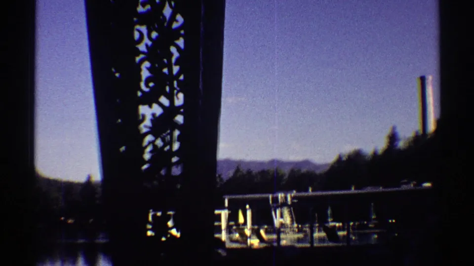 1969 Colorado 8mm frame with a bridge edge in shadow and a marina with boats, docks, trees, and mountains beyond.