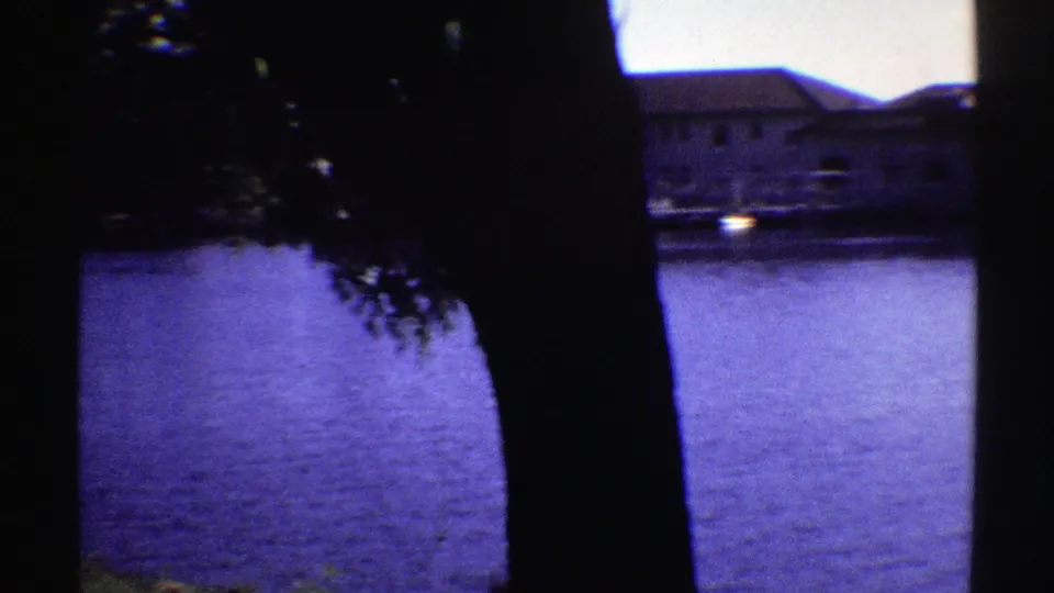 1969 Colorado lake view with foreground tree silhouettes, blue-tinted water, and low buildings across the shoreline.