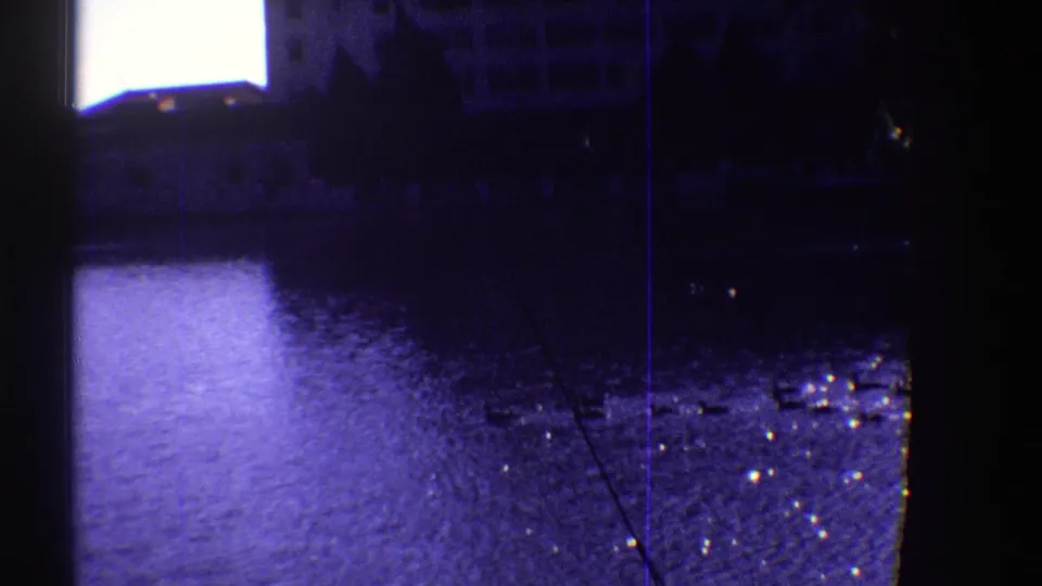 1969 Colorado 8mm frame showing ducks on rippling floodwater, with bright glare, dark foreground edges, and faint town structures in the background.
