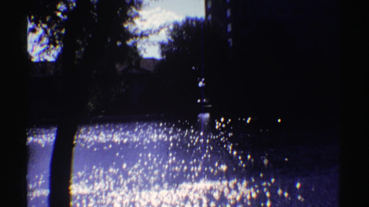 1969 Colorado 8mm frame with bright glare on water, shaded trees, and a partially visible bank beyond.