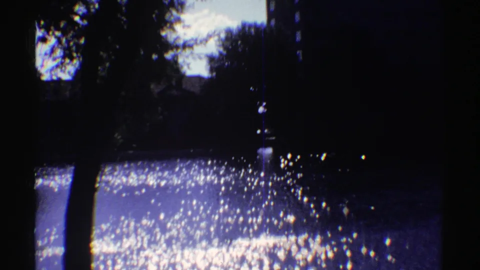 1969 Colorado 8mm frame with bright glare on water, shaded trees, and a partially visible bank beyond.