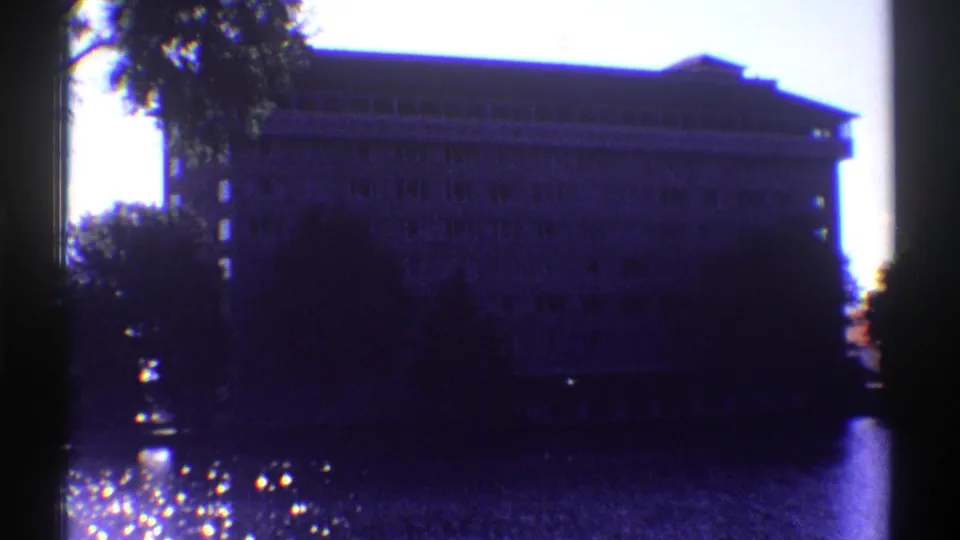 1969 Colorado frame showing a large multi-story building across water, partly obscured by tree trunks and heavy shadow.