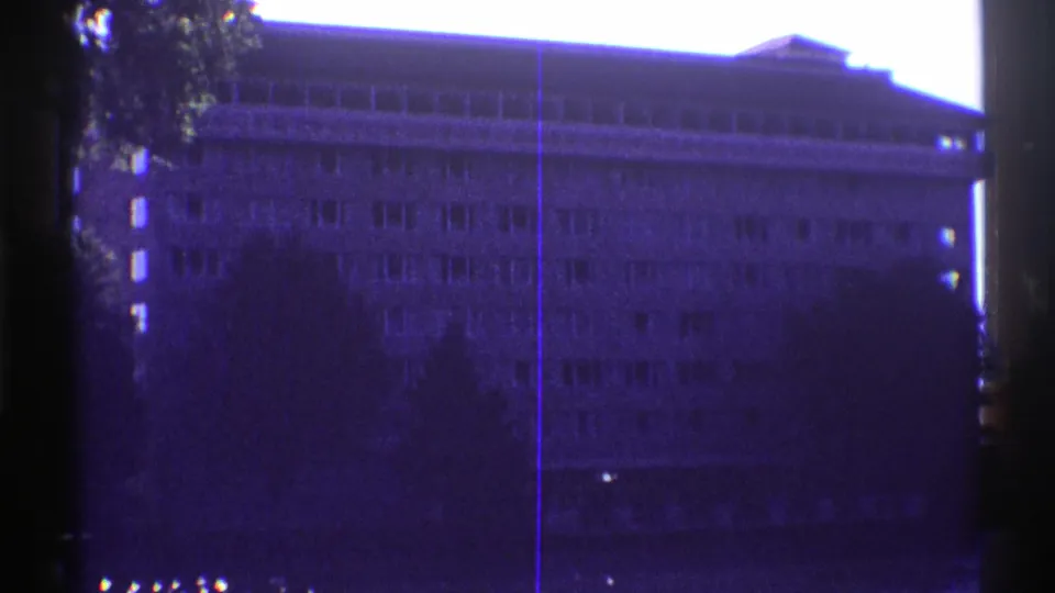 Late-1960s 8mm view of an unidentified Colorado building facade across water, with silhouetted trees and visible film scratches.