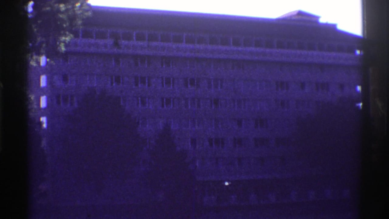 1969 Colorado 8mm frame showing a large multi-story building facade partly obscured by a tree and dark film edges.