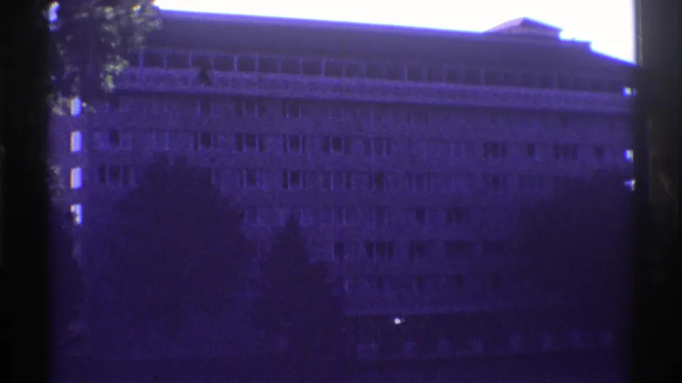 1969 Colorado 8mm frame showing a large multi-story building facade partly obscured by a tree and dark film edges.