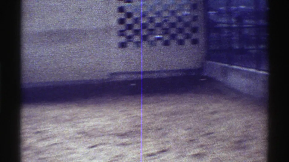 1969 Colorado 8mm frame showing the sandy animal enclosure after the giraffe has moved mostly out of view, with wall and vent details visible.