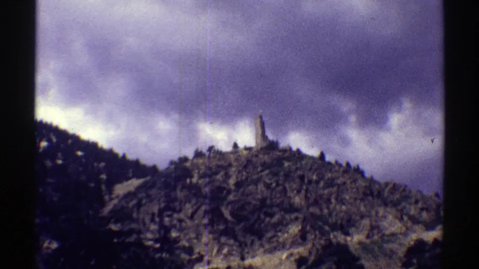 A 1969 Colorado hillside scene shows trees, cloud cover and a narrow ridge-top structure in soft 8mm color.