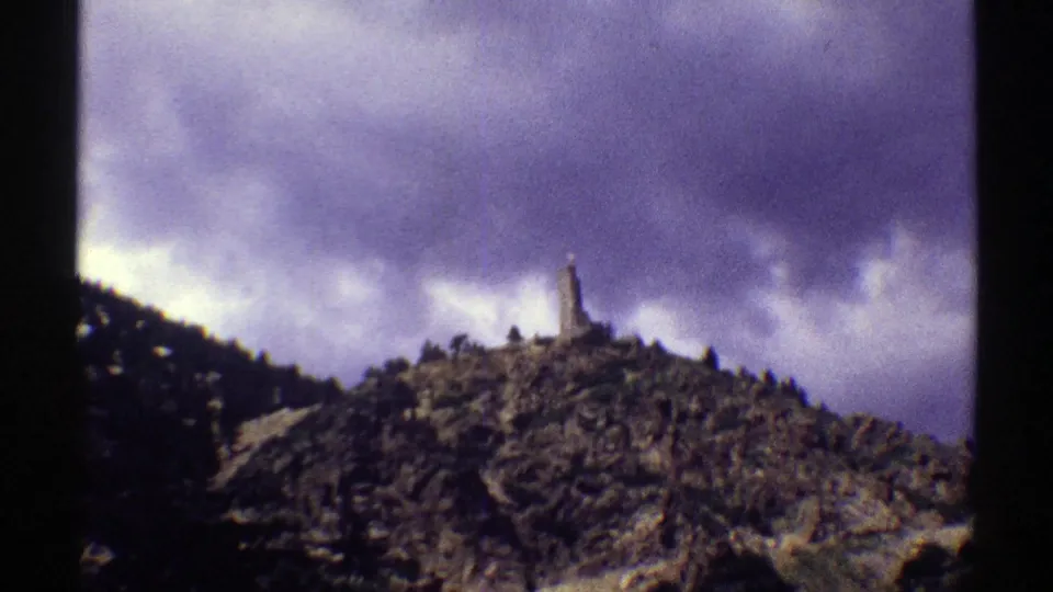 The frame holds on a Colorado hill under heavy clouds, with a small upright structure visible along the ridge.