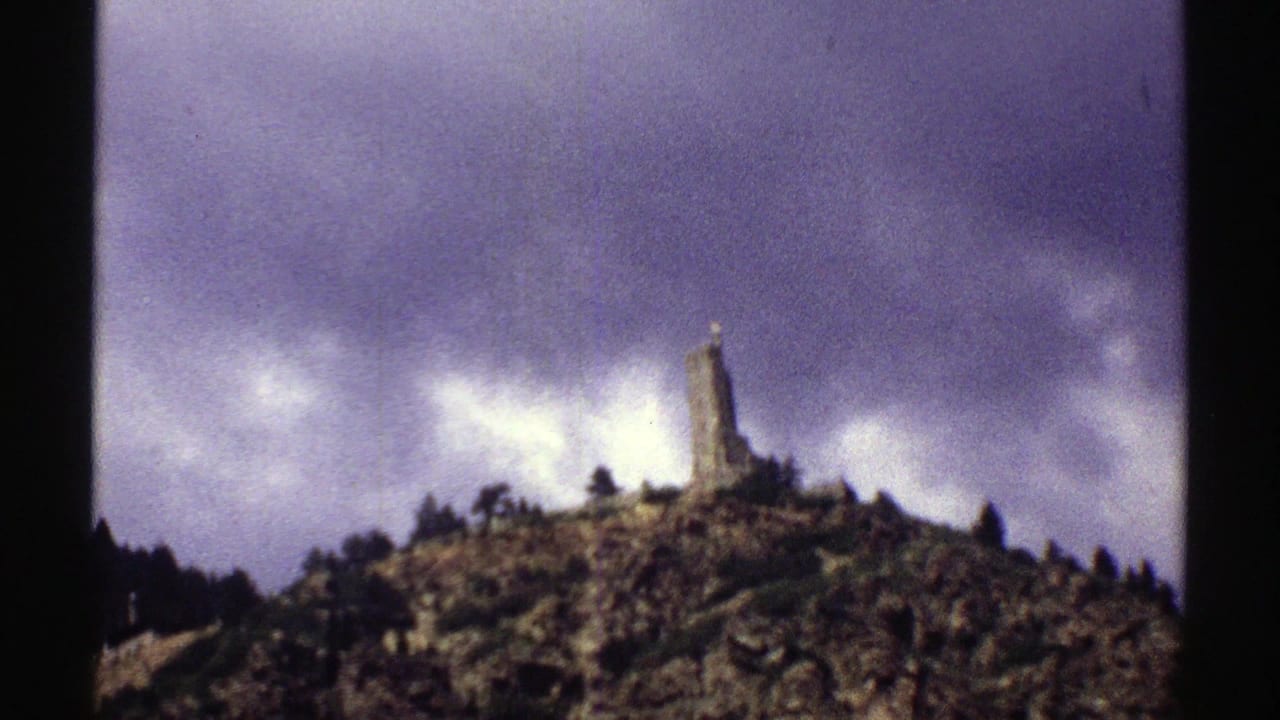 1969 Colorado 8mm frame showing a distant stone monument atop a rocky, tree-dotted hill under heavy clouds.