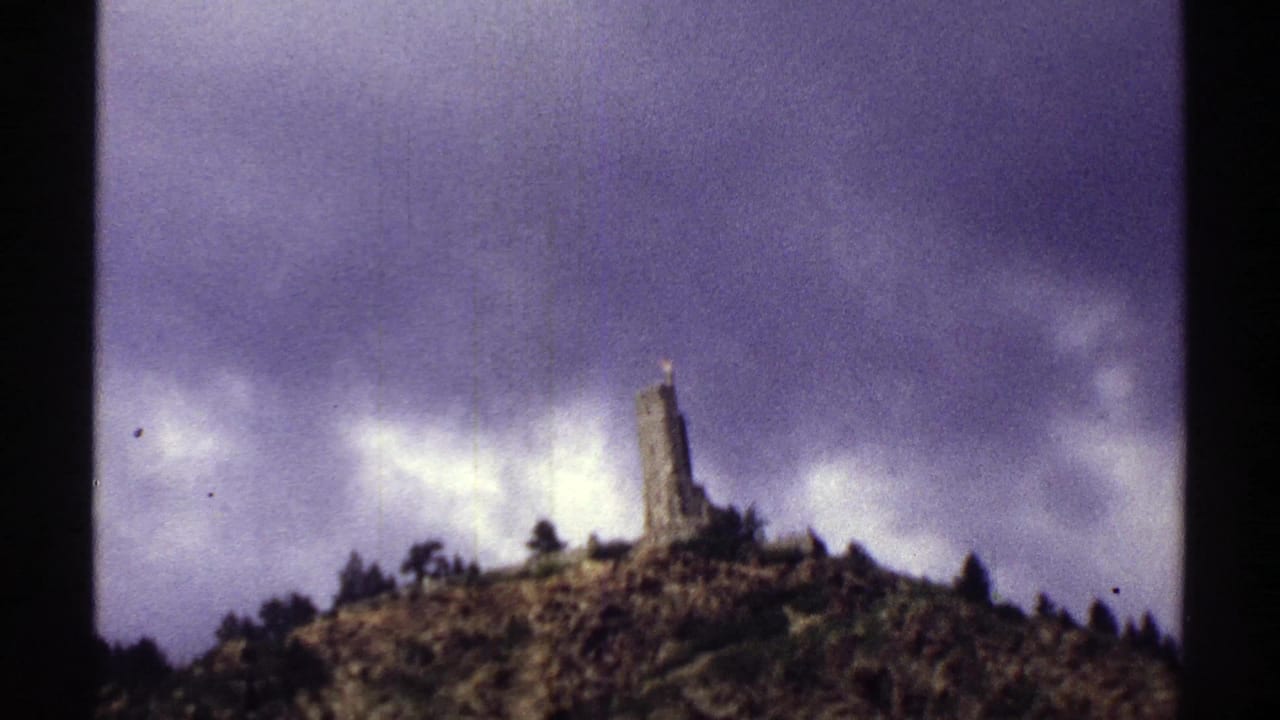 Distant hilltop stone monument framed by clouds and rocky terrain.