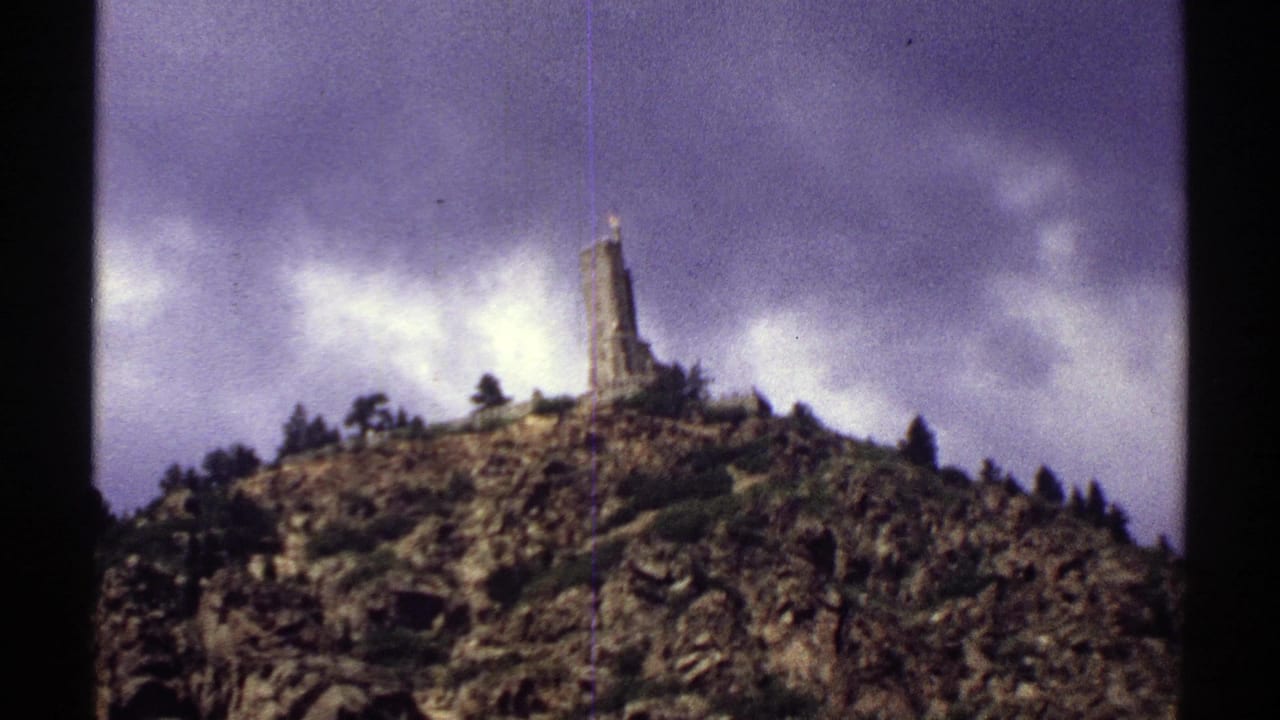 1969 Colorado 8mm frame showing a rugged mountain summit topped by a tower beneath a dramatic cloudy sky.