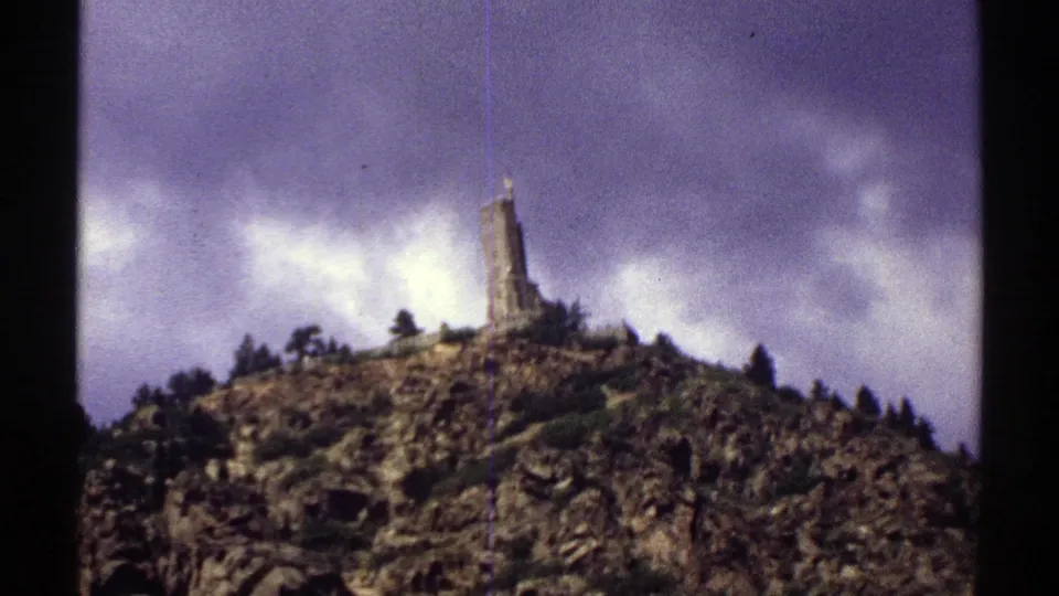 1969 Colorado 8mm frame showing a rugged mountain summit topped by a tower beneath a dramatic cloudy sky.