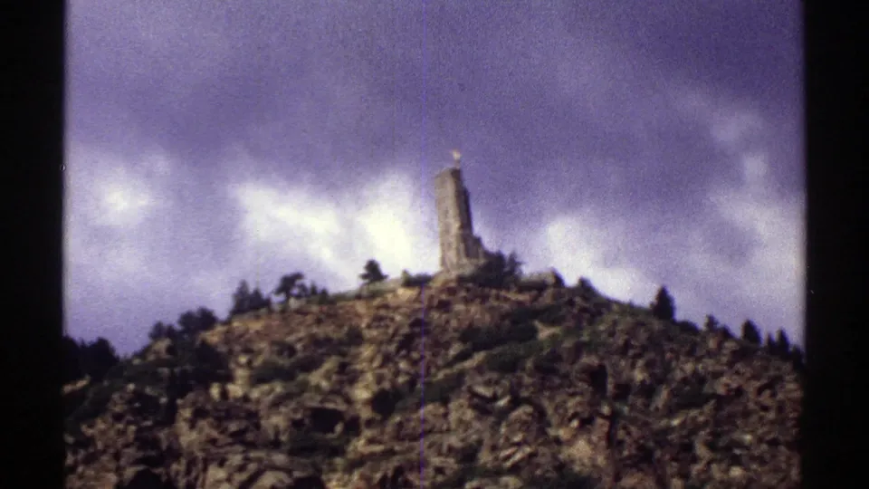 1969 Colorado home-movie frame of a tower on a rugged ridge, seen through soft 8mm color and grain.