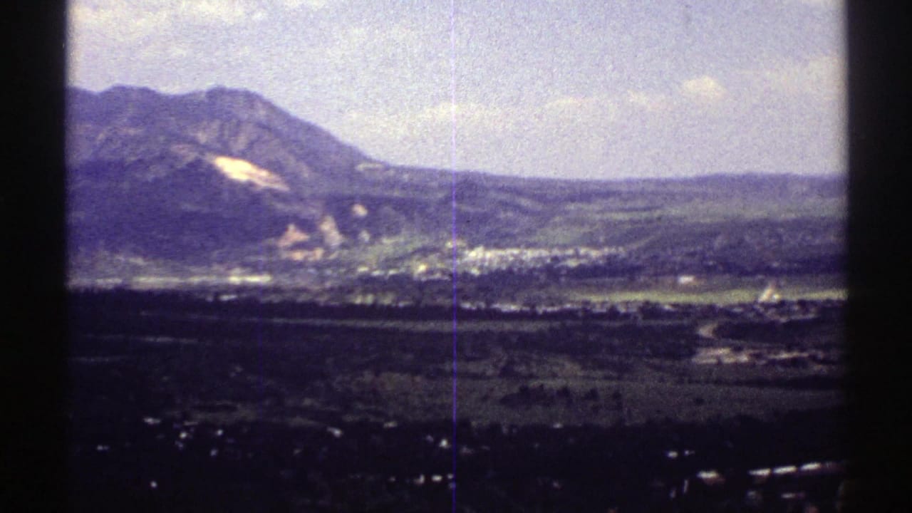 1969 Colorado landscape view with a mountain ridge, pale hillside area, scattered buildings, and open valley fields.