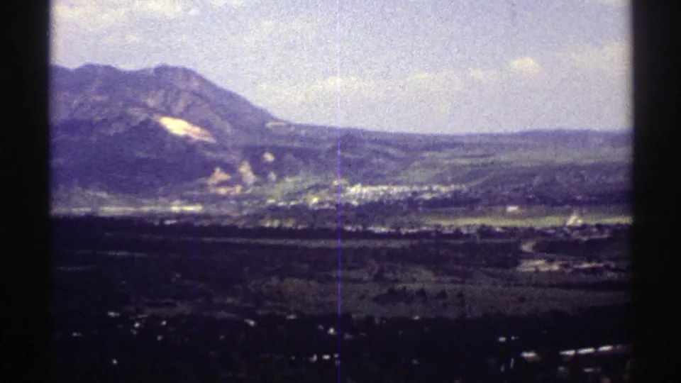 1969 Colorado landscape view with a mountain ridge, pale hillside area, scattered buildings, and open valley fields.