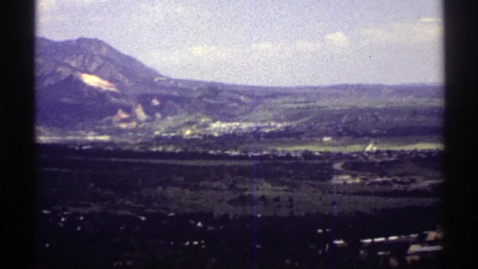 Colorado home-movie frame from 1969 showing the mountain slope at left and a distant town spread across the valley.