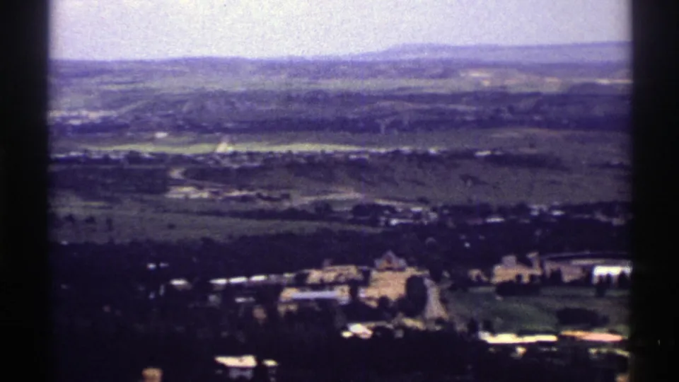 1969 Colorado 8mm frame showing a broad valley, low hills, distant buildings, and foreground structures from an elevated viewpoint.