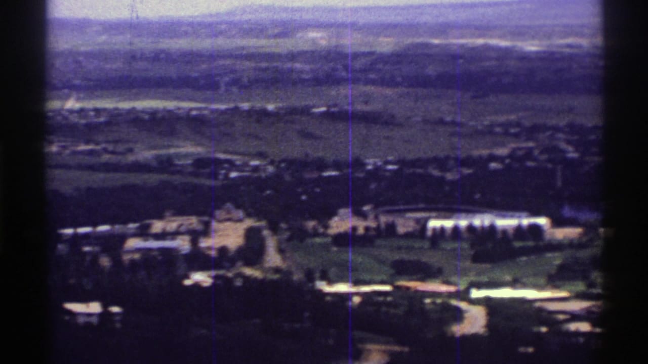 1969 Colorado home-movie frame showing a distant elevated view of fields, trees, low buildings, and a hazy horizon.