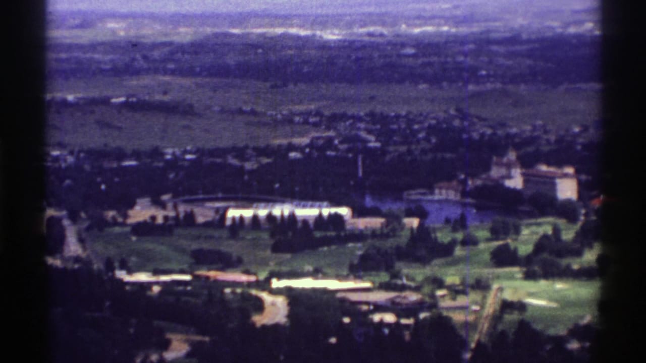 Green grounds with low buildings, roads or paths, trees, and distant fields.