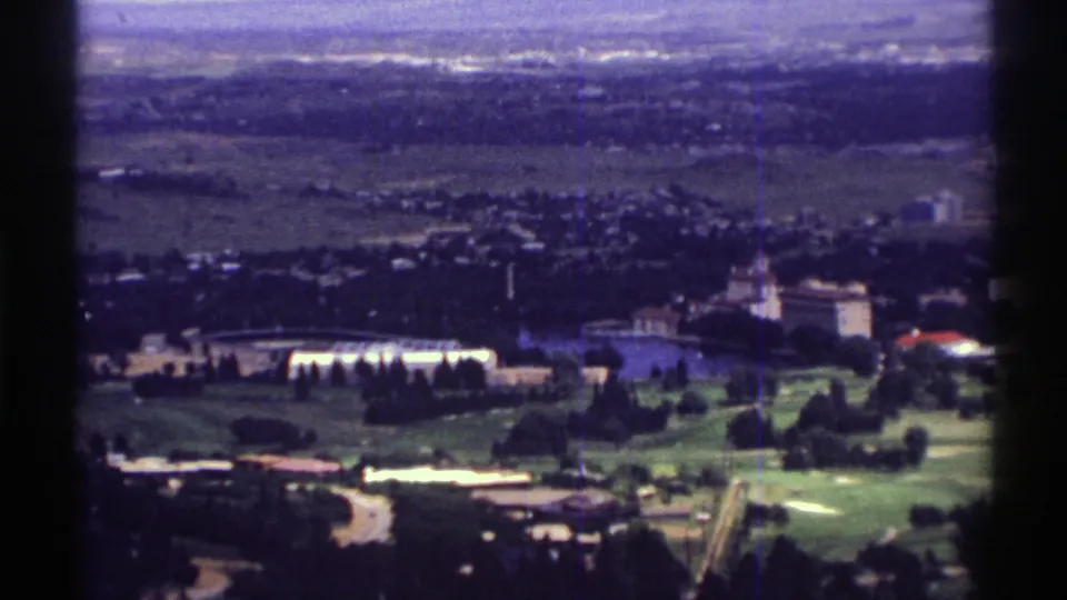 1969 Colorado elevated home-movie view showing buildings, trees, open lawns, and broad fields behind a town area.