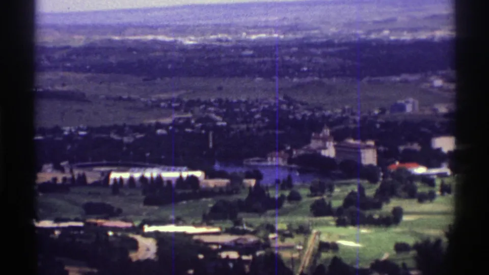 1969 Colorado frame showing a distant town landscape with low buildings, green lawns, trees, and open land beyond.