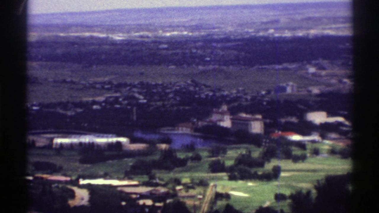 1969 Colorado 8mm frame looking across green fields, scattered trees, roads and a distant townscape from an elevated viewpoint.