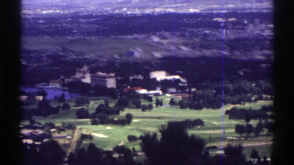 1969 Colorado 8mm view across open green land toward low buildings and a distant settlement, with visible vertical film wear.