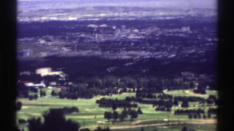 1969 Colorado frame with a wider elevated look over green fields, tree lines and a hazy town area beyond.