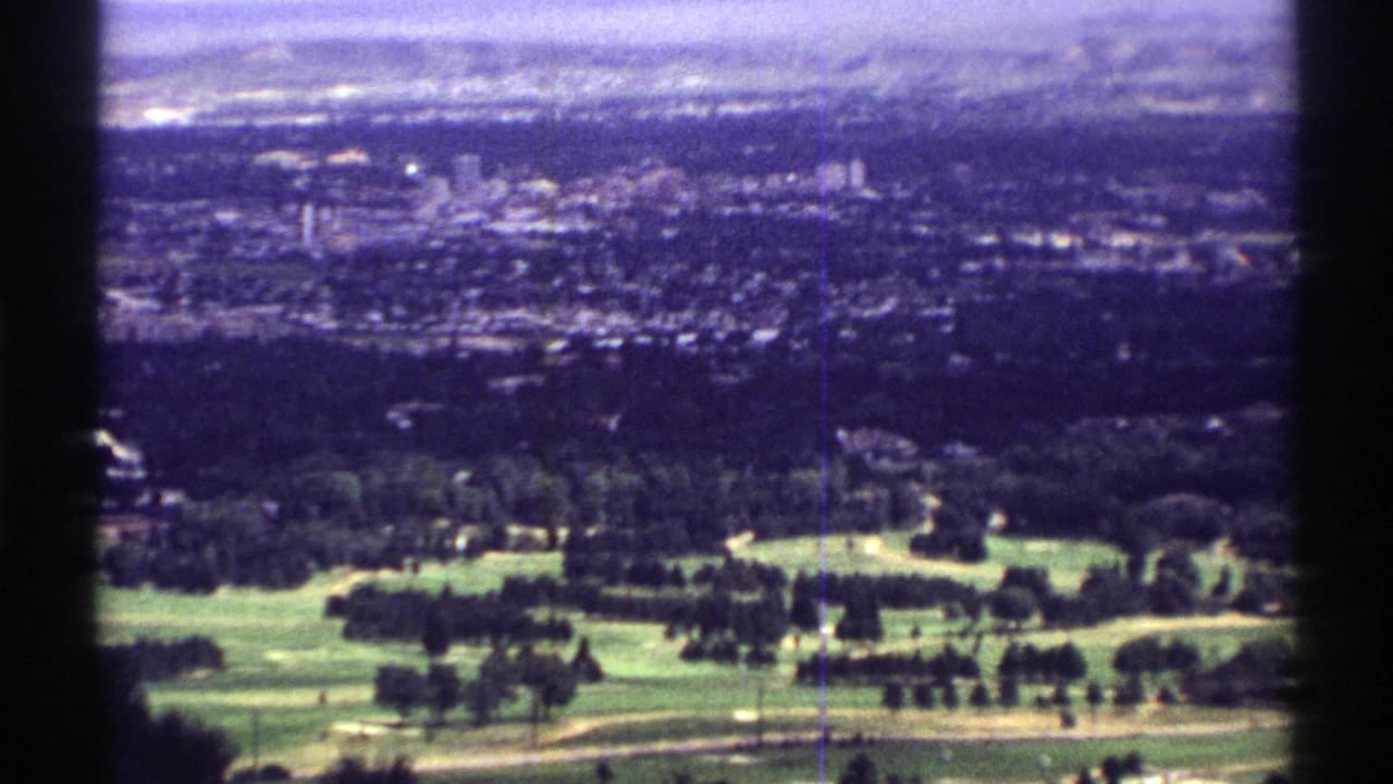 1969 Colorado 8mm frame showing a golf course in the foreground and a hazy suburban town beyond.