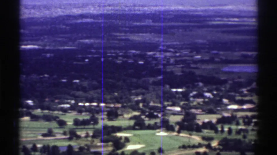 1969 Colorado home-movie frame with golf-course greens, nearby homes, and a broad hazy suburban distance.