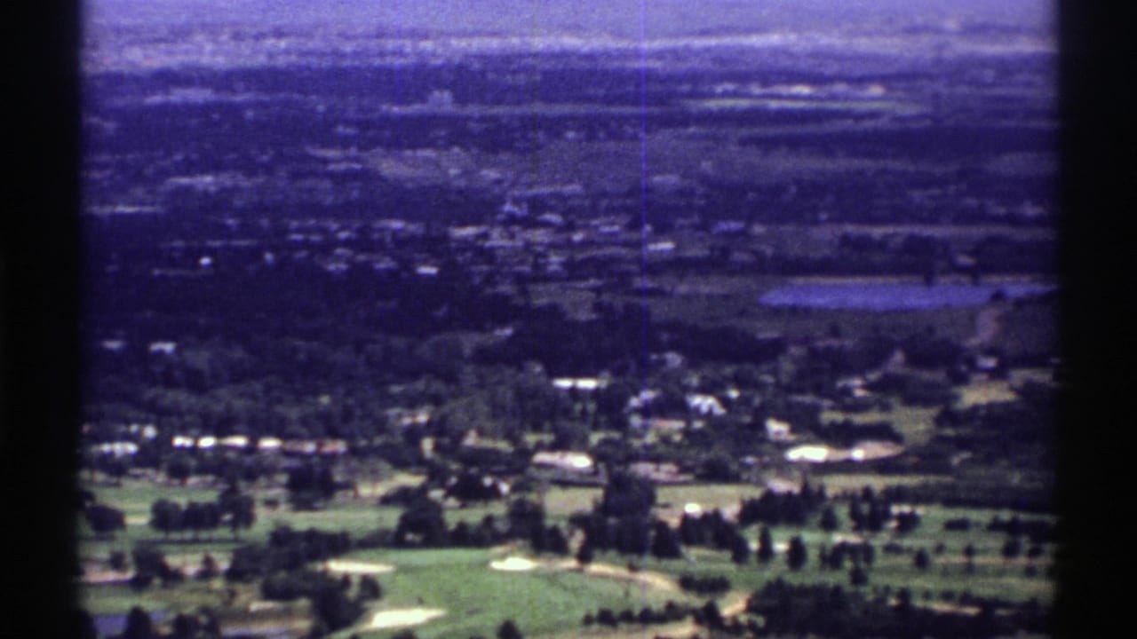 1969 Colorado 8mm frame showing a high view across a golf-course-like foreground toward houses, fields, and hazy hills.
